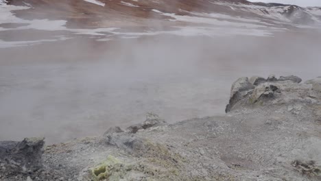 pale yellow steam vent push vapor into orange icelandic valley on windy day