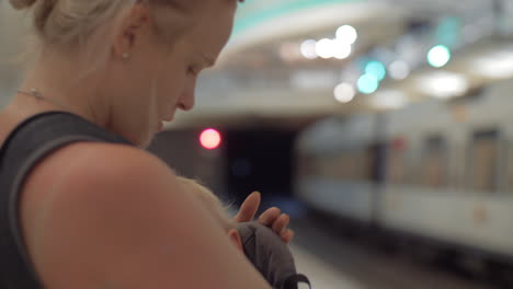 mamá con el niño durmiendo en el portero del bebé esperando el tren del metro