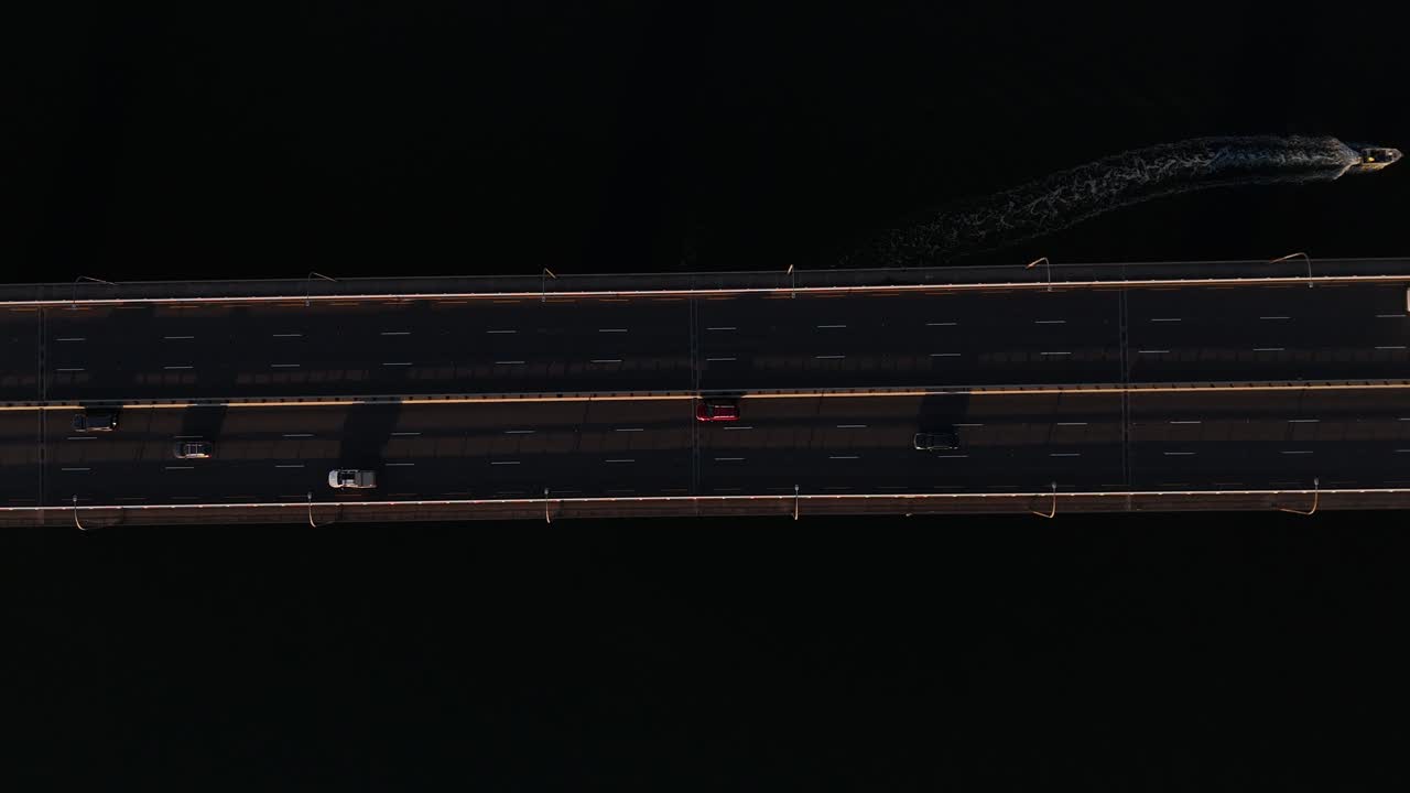 Drone top down ascend above visible traffic as cars and boats drive along bridge, motion over calm water in Sydney NSW Australia