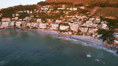 Clifton-beach-coastline-full-of-tourists-and-hotels-in-Cape-Town-at-sunset,-aerial