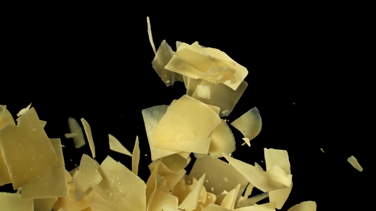 Primo piano al rallentatore di scaglie di Parmigiano che cadono su sfondo nero.