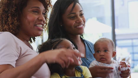 multi-generation female african american family sitting on sofa at home watching tv together