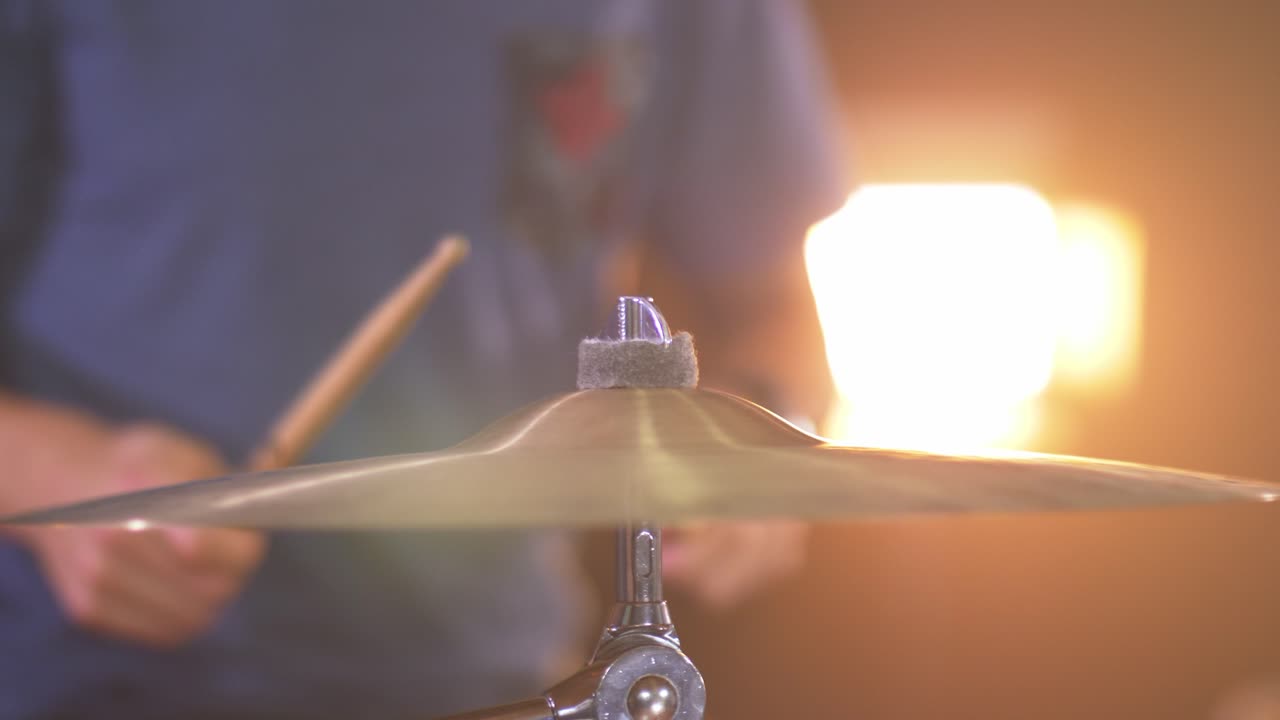 primer plano de un baterista profesional tocando un redoble de tambor en un platillo de paseo con una cálida luz led en el fondo