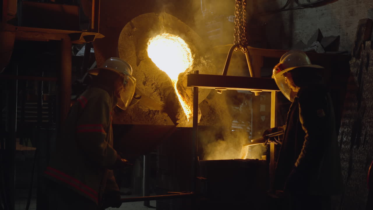 Fiery blast furnace at foundry with workers handling molten metal