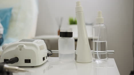 close-up view of essential tools and bottles arranged neatly on white table, including electric device, spray bottles, and containers, with blurred background showing green indoor plant