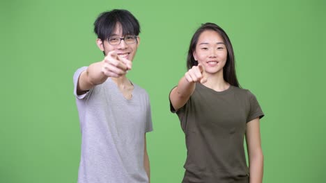 young asian couple pointing at camera