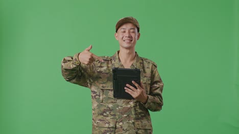 asian man soldier smiling and pointing to a tablet in his hand while standing in the green screen background studio