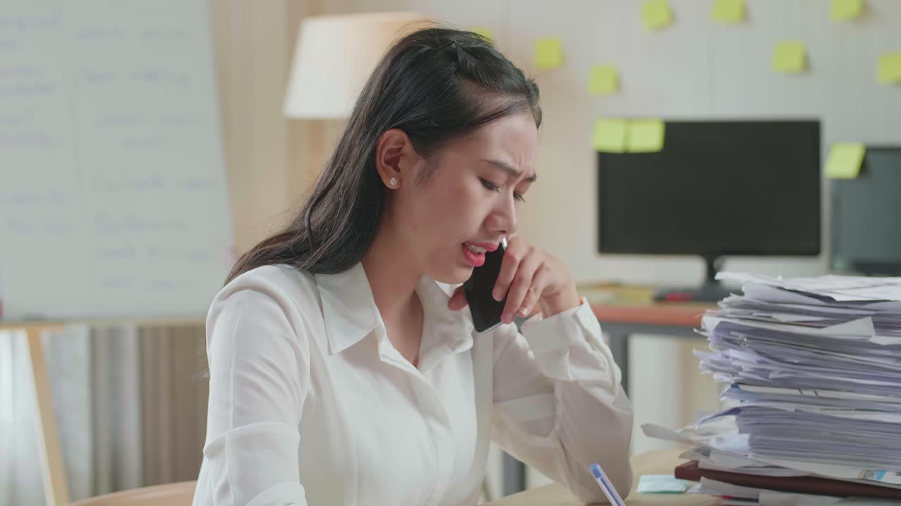 사무실에서 문서와 함께 열심히 일하는 동안 전화로 이야기하고 메모를 취하는 아시아 여성의 클로즈업