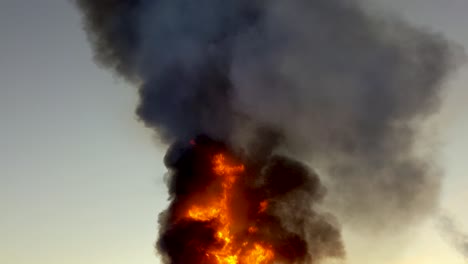 huge raging oil fire sends thick black smoke billowing into the atmosphere while the sun rises in the background