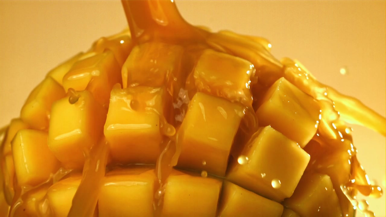 Versamento al rallentatore di sciroppo dorato su mango fresco a cubetti