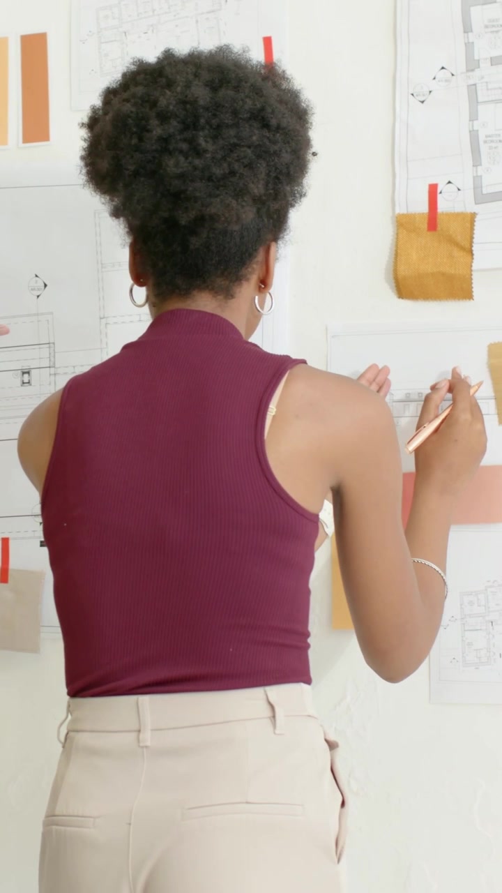 Vertical video: Reacting to plans, maroon designer adjusting swatches at studio wall for review