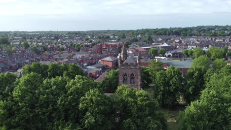 Aerial-view-rising-above-rural-English-town-woodland-countryside-idyllic-church-bell-tower-and-graveyard