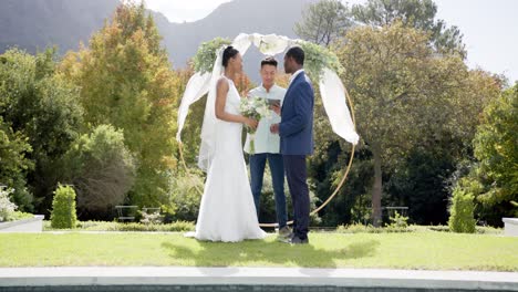 Hombre-Birracial-Oficiando-El-Matrimonio-De-Una-Feliz-Pareja-Afroamericana-En-Un-Jardín-Soleado,-En-Cámara-Lenta