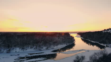 sunset over frozen river and evergreen forest. country highway passing across water at winter season.