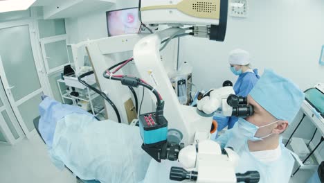 surgeon looking into the microscope at the eye of female patient at the operating room. doctor using microscope during eye surgery process, treatment of cataract and diopter correction.