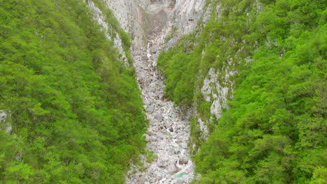 aerial footage of a waterfall and river going through a green and steep canyon in slovenia