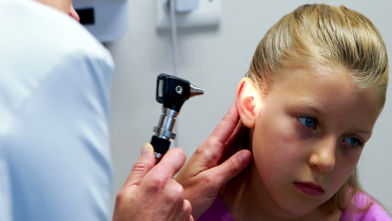 una mujer examinando el oído del paciente con un otoscopio