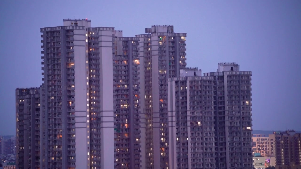 Tomada de revelação com movimento de câmera para cima de um edifício de apartamentos arranha-céu com poucas luzes acesas, mostrando a vida congestionada em complexos de apartamentos em Gurgaon, Delhi, Bangalore, Mumbai.