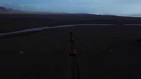 aerial landscape view of bright red quad bikes crossing a river off road on iceland black sand beach