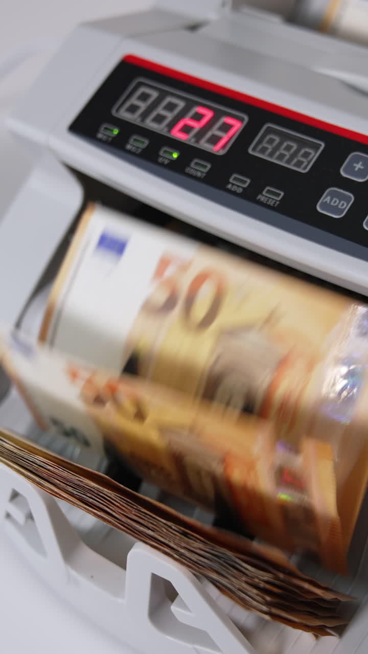 Hand puts a pack of fifty euro bills into money counting equipment. Machine for calculating currency at work close up. Blurred backdrop. Vertical video