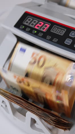 hand puts a pack of fifty euro bills into money counting equipment. machine for calculating currency at work close up. blurred backdrop. vertical video