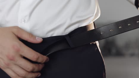 신부는 벨트를 착용합니다.  셔츠를 입은 남자는 결혼식 아침에 바지를 벨트를 입습니다.