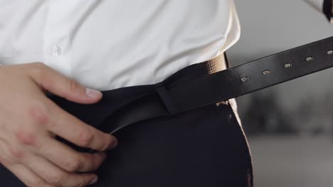 groom wears a belt. man in white shirt puts belt on his pants in wedding morning