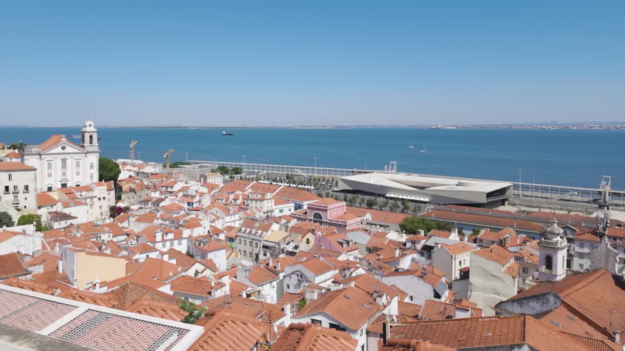 Traditional orange rooftops, church tower, and modern MAAT Museum by Tagus River in Lisbon, Portugal, creating a blend of historical and contemporary architecture. Pan right
