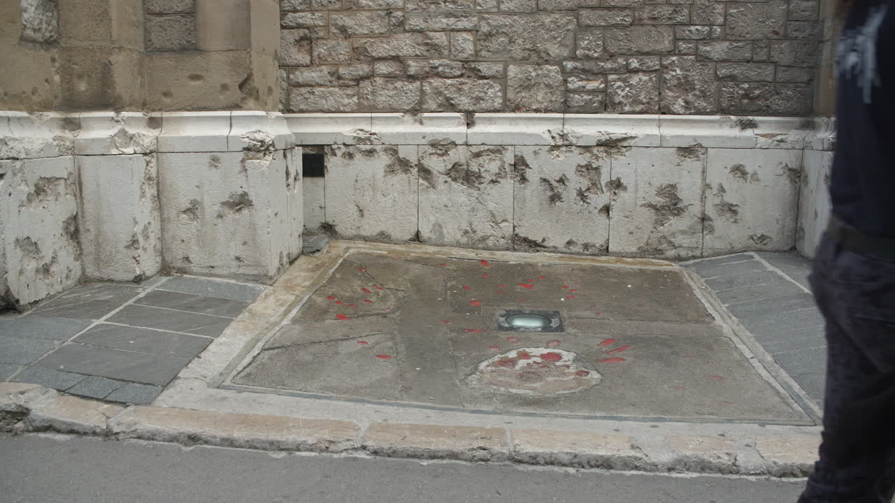People walk in front of a Sarajevo rose war memorial signifying where three or more were killed in mortar shelling, exterior of chapel in Sarajevo, Bosnia and Herzegovina
