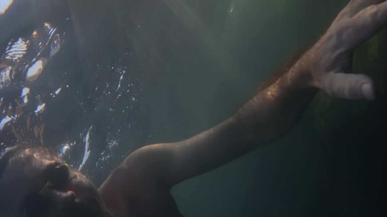 Person swimming under shimmering water, sun light reflecting and creating ripples on the clear blue surface. Serene underwater view