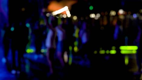 crowd or group of people dancing in an open air club with colorful lights.