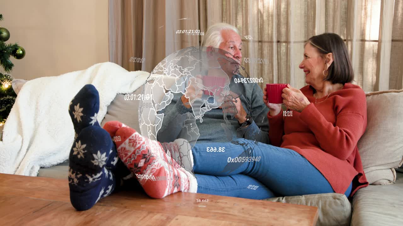 Senior couple sharing holiday chat, sipping mugs, globe appearing over couple rotating tech data