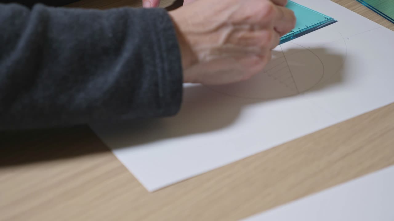 mano femenina haciendo un dibujo geométrico en una hoja de papel con un lápiz y un cuadrado establecido