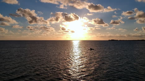 silueta de una persona en kayak en el océano durante la puesta del sol, en órbita aérea a la izquierda