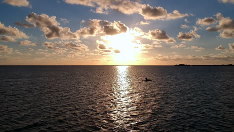 silhouette of person kayaking in the ocean during sunset, aerial orbiting left