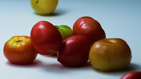 más tomates pequeños cayendo en tomates de carne más grandes en una mesa blanca