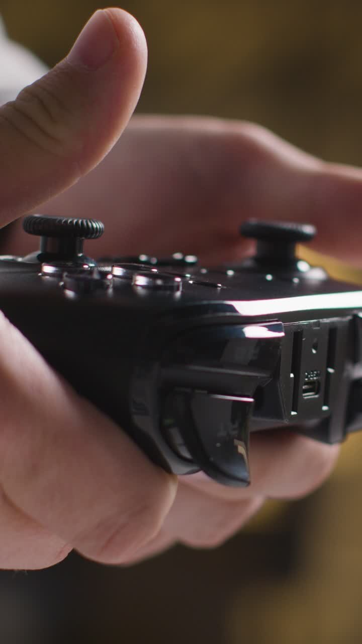 Video verticale: Primo piano laterale, mani di un uomo che gioca con un controller di videogiochi, ripresa 1