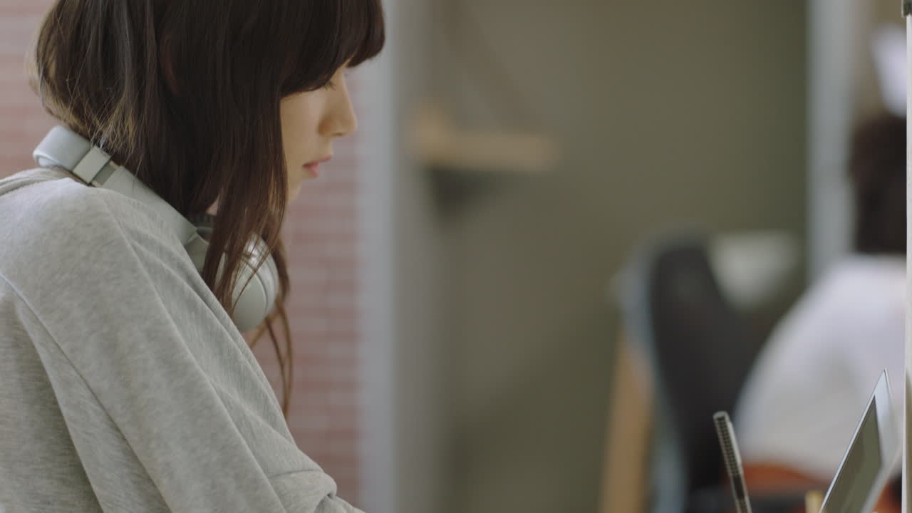 젊은 아시아 사업가 여성이 노트북 컴퓨터를 사용하여 프로젝트를 진행하고 주스를 마시고 바쁜 사무실에서 창의적인 프로젝트를 즐기고 있습니다.