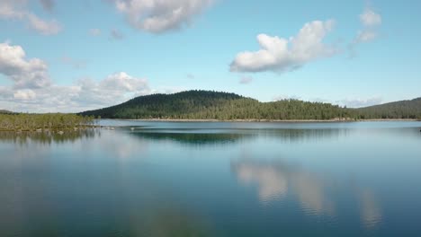 forward aerial shot over a calm lake in finland with clouds reflected in it