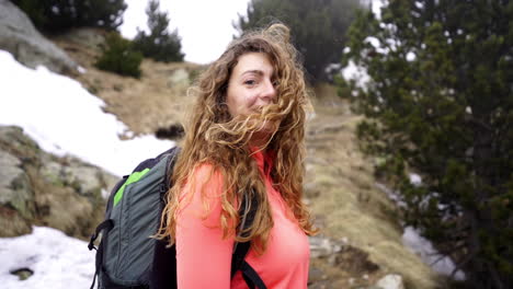 slow motion portrait of young happy caucasian woman long blond hair blowing in the wind while backpacking trekking hiking high altitude mountain with snow trails in wilderness