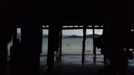 Silhouette-Von-Zwei-Jungen-Menschen,-Die-Sich-Unter-Den-Docks-Am-Strand-Schleichen