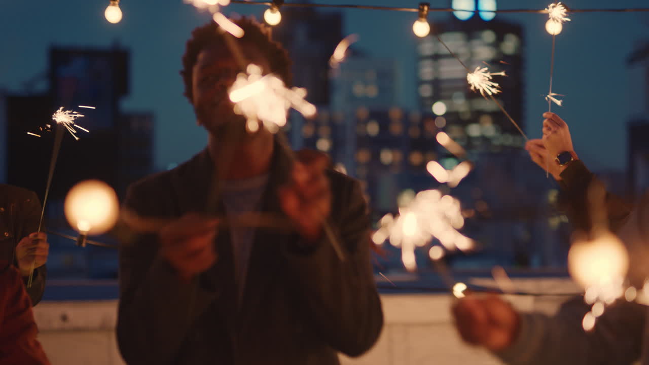 cheerful group of friends holding sparklers celebrating new years eve on rooftop at night having fun dancing enjoying holiday party celebration diverse young people waving festive fireworks