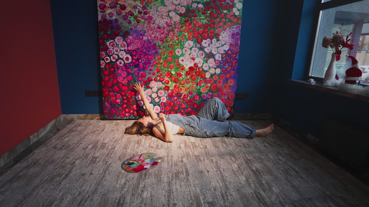 Mujer joven tumbada en el suelo contemplando una pintura floral vibrante