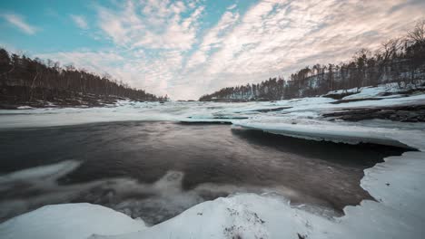 frozen river partially melting, flowing under ice layers at målselvfossen, timelapse