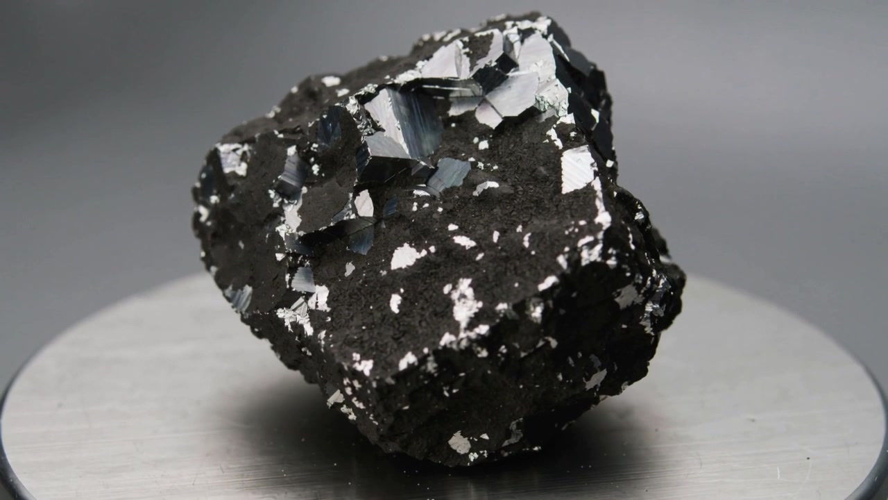Roca giratoria revelando escamas metálicas para mostrar facetas de cristal en un soporte cuando la cámara arranca, iluminación