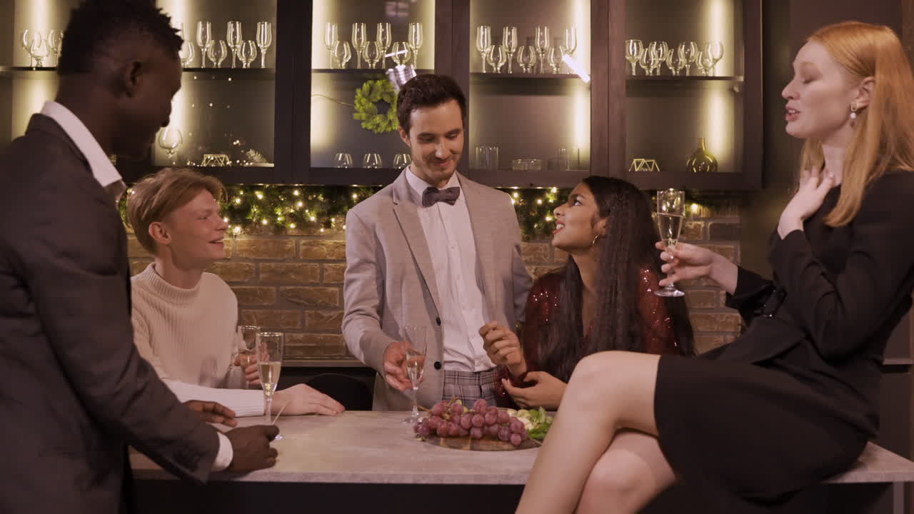 신년 파티를 축하하는 우아한 옷을 입은 친구들, 샴페인을 마시고 포도를 먹으면서 바 카운터 주위에 서 있다