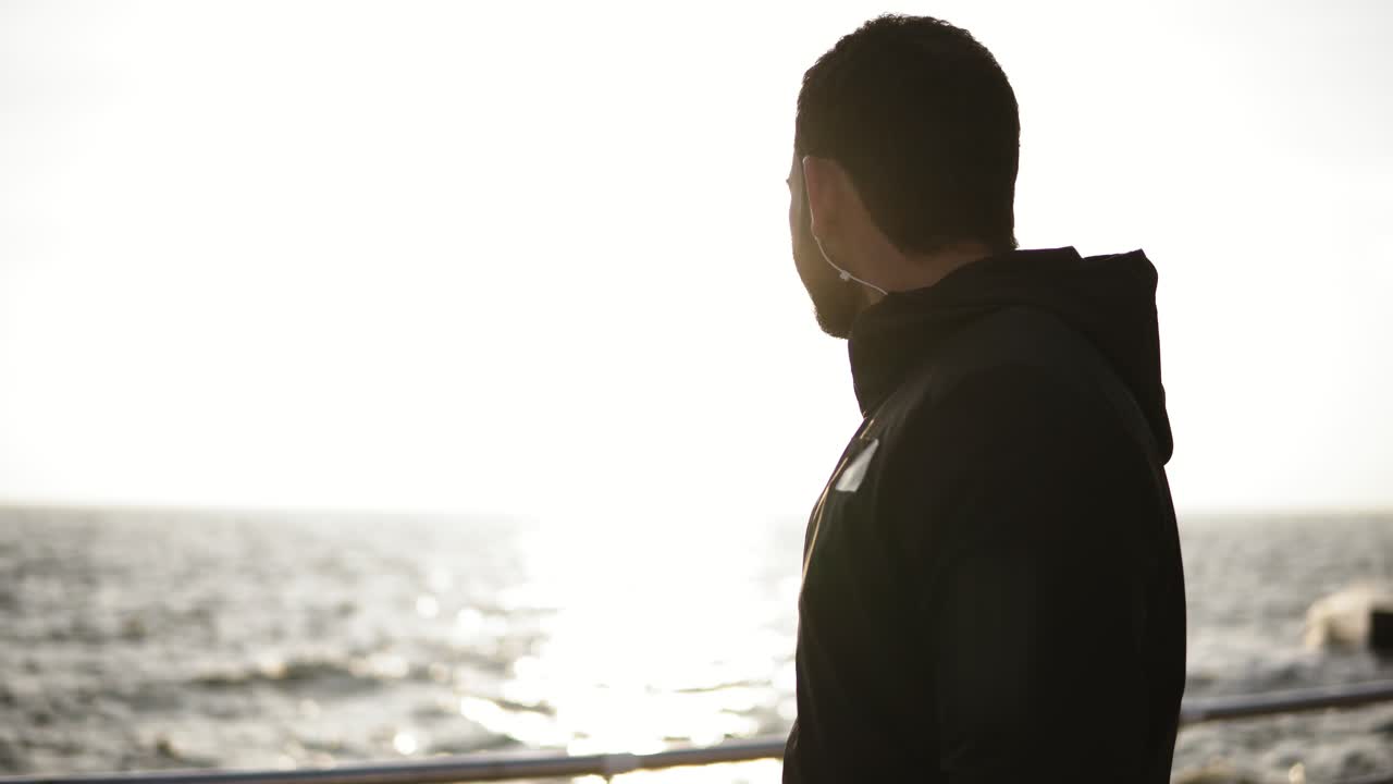 운동 후 헤드폰을 끼고 플라스틱 피트니스 병에서 물을 마시는 매력적인 젊은 남성. 스포츠, 피트니스, 청소년 복지.