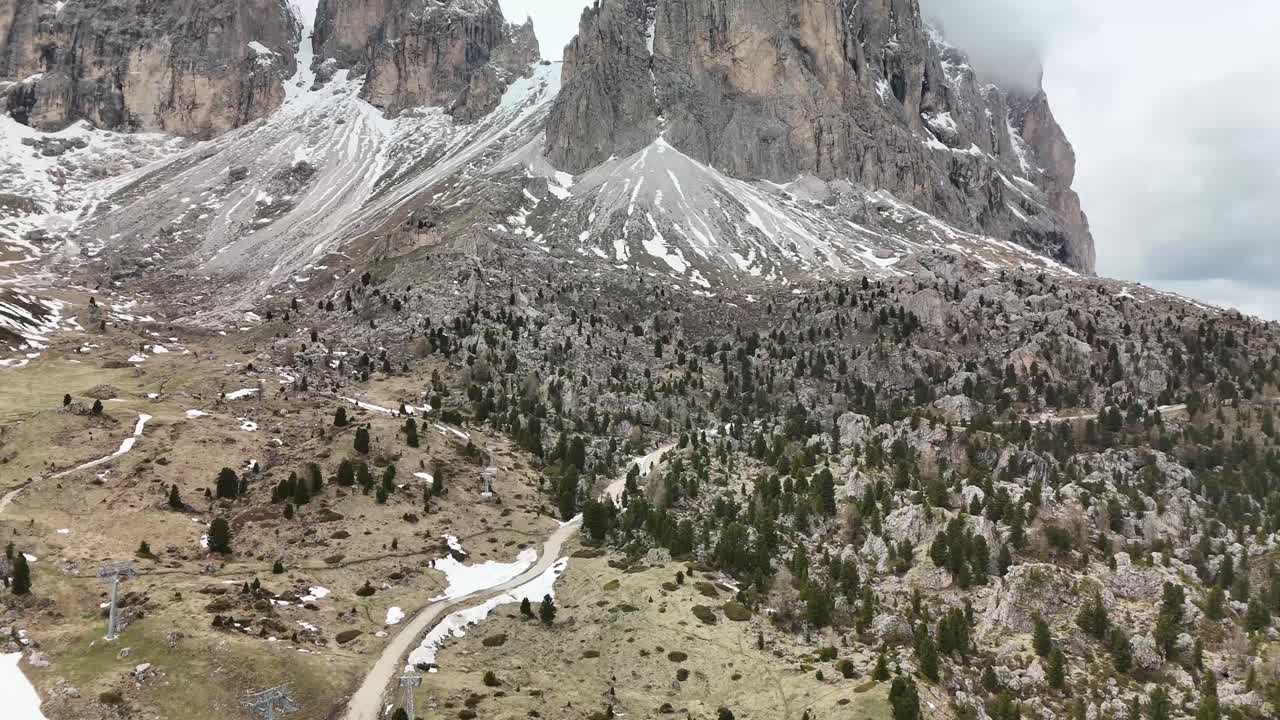 Aerial perspective of the Sassolungo (Langkofel) mountain group in the Dolomites, Italy. From high above the mountain path, the dramatic peaks rise into swirling clouds, the Italian Alps