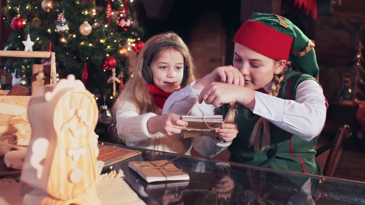 Girl with Santa Claus elf bandit letters to children in a room with a fireplace and a Christmas tree