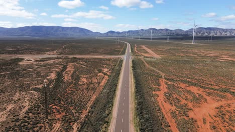 Drone-aerial-over-Australian-desert-country-road-near-renewable-energy-wind-farm-with-car-driving-mountains-in-background